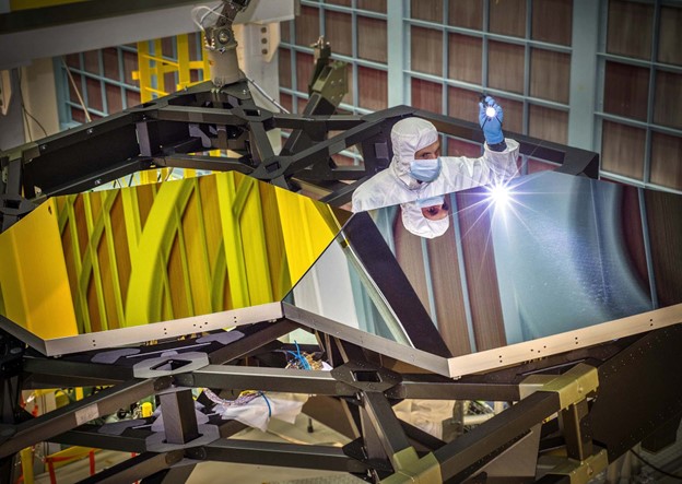An engineer examines test mirror segments in the clean room of NASA’s Goddard Space Flight Center in Maryland; a technician helps to pack up the sunshield for the final time in February 2021. Northrop Grumman The Webb team is busy rehearsing the routines they’ll execute 24/7 out of Baltimore during Webb’s monthlong journey to Lagrange point 2, followed by its five-month commissioning period. “Do I feel confident?” said Menzel. “Yes. I feel confident that we’ve done everything we possibly could. The risk is acceptably low. It’s as good as it’s going to be. And I’m pretty confident that we’re going to do fine.  “Could something go wrong? Hell, yeah.” Reasonable Guesses Once the Hubble got working, humanity soaked up the sight of the cosmos like near-sighted kids wearing glasses for the first time. We also learned there was stuff out there that we couldn’t see.  In 1998, two rival teams of astronomers used the Hubble along with other telescopes to observe supernovas in distant galaxies and ascertain that the expansion of the universe is accelerating. This exposed the existence of an accelerating agent infusing all of space, known as dark energy. There’s so much space that dark energy makes up 70% of everything. (Another 26% is dark matter, and 4% is luminous atoms and radiation.)  Other puzzles soon turned up. The astronomer Wendy Freedman used Hubble to observe pulsating stars called cepheids. From these, in 2001 she and her team measured how fast the universe is currently expanding, achieving 10% accuracy, a huge improvement over previous measurements. In the years since Freedman’s measurement, the cosmic expansion rate has landed at the center of the biggest controversy in cosmology. The issue is that, based on the universe’s known ingredients and governing equations, theorists infer that space should currently be expanding more slowly than the measurements suggest. Its fast expansion may point to additional unknown ingredients in the cosmos beyond dark matter and dark energy. But Freedman, who is calm and authoritative, isn’t convinced yet that the measurements are right. She’ll lead a team that will use the Webb telescope to scrutinize cepheids and other stars more closely; they hope to measure the expansion rate precisely enough to tell for sure whether there’s an exotic fundamental ingredient afoot.
